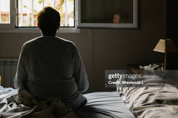 retired elderly woman sitting on bed at home - krankenbett stock-fotos und bilder