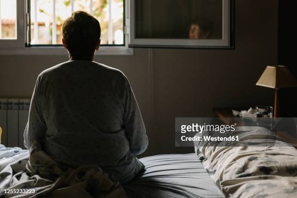 retired elderly woman sitting on bed at home - illness fotografías e imágenes de stock