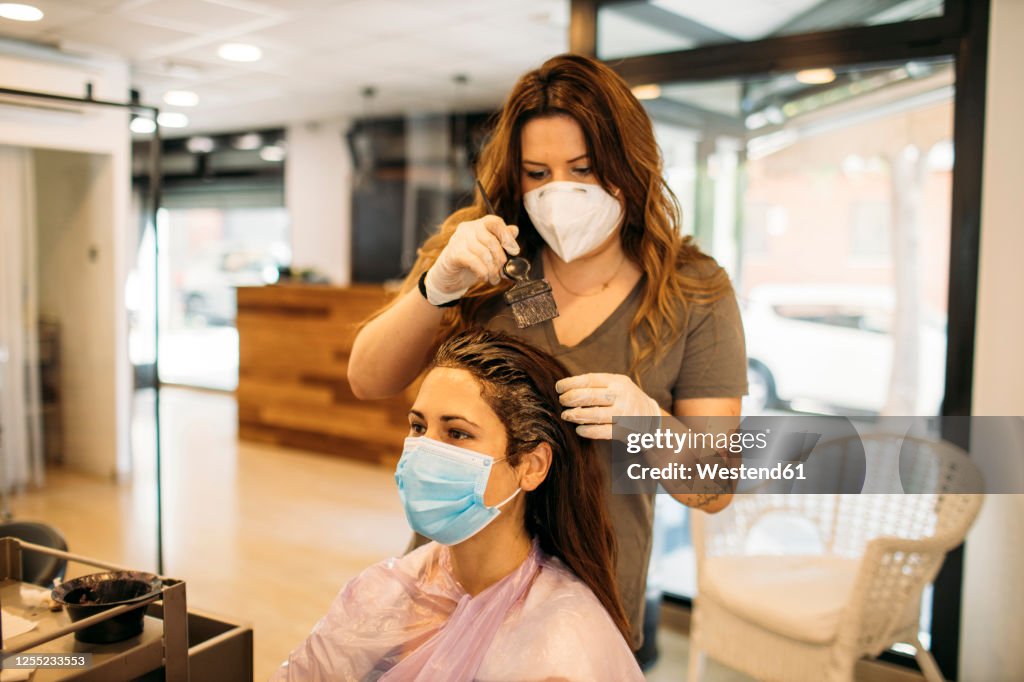 Female hairdresser with mask staining hair of female customer with mask