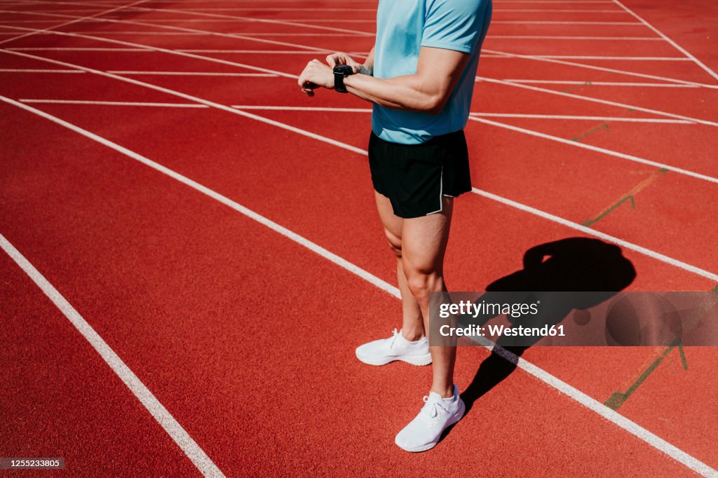 Male athlete on tartan track checking smartwatch