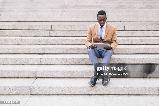 young businessman sitting on stairs using a tablet - well dressed stockfoto's en -beelden