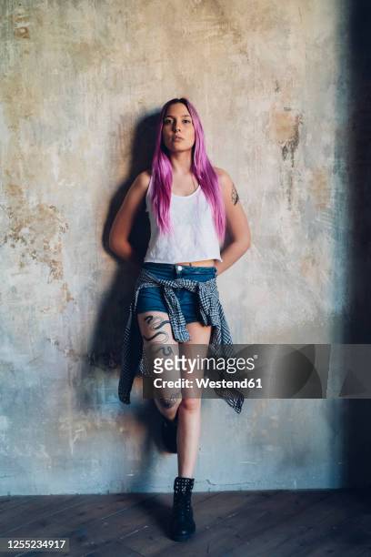 portrait of a stylish young woman with pink hair leaning against a wall - short hair photos et images de collection