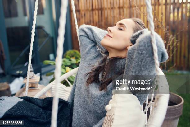 young woman with eyes closed relaxing on swing in garden - hände hinter dem kopf stock-fotos und bilder