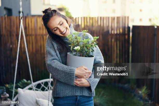 cheerful woman carrying potted plant while standing in yard - topfpflanze stock-fotos und bilder