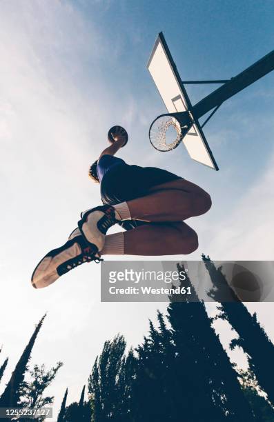 directly below view of teenage player dunking ball in basketball hoop against sky - sport di squadra foto e immagini stock