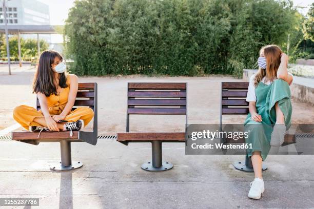 two friends wearing protective masks meeting outdoors during corona crisis and keeping distance - social distancing friends stock pictures, royalty-free photos & images