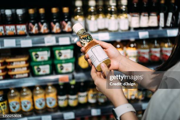 cropped shot of young asian woman groceries shopping in a supermarket. standing by a produce aisle, holding a bottle of organic cooking oil and reading nutritional label - seasoning ストックフォトと画像