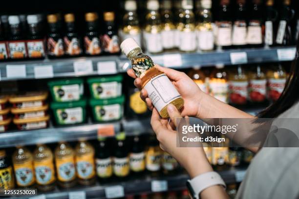 cropped shot of young asian woman groceries shopping in a supermarket. standing by a produce aisle, holding a bottle of organic cooking oil and reading nutritional label - food staple stock pictures, royalty-free photos & images