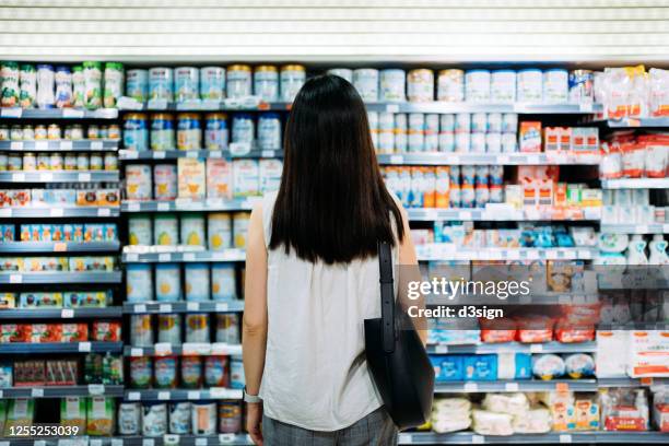 rear view of young asian mother groceries shopping for baby products in a supermarket. she is standing in front of the baby product aisle and have no idea which product to choose from - 生鮮食品コーナー ストックフォトと画像