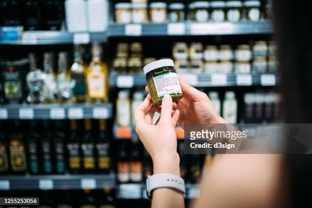 cropped shot of young asian woman groceries shopping in a supermarket. standing by a produce aisle, holding a bottle of organic cooking sauce and reading nutritional label - use by label bildbanksfoton och bilder