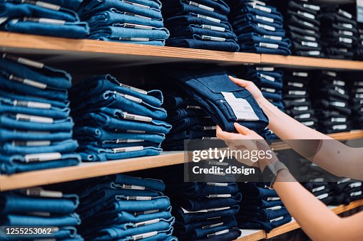 Cropped shot of woman's hand selecting a pair of trousers from the display shelf while shopping in a clothing store in the city Cropped shot of woman's hand selecting a pair of trousers from the display shelf while shopping in a clothing store in the city