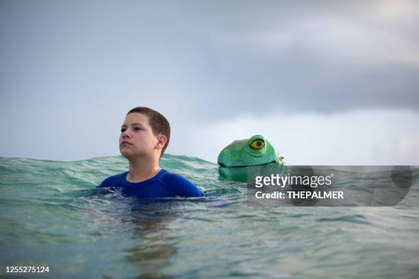 jovencito en la playa mientras un lagarto acecha en el fondo - marine iguana fotografías e imágenes de stock