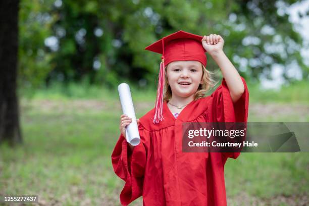graduado de preescolar levanta el brazo en celebración por completar el año escolar - kids in graduation gowns fotografías e imágenes de stock