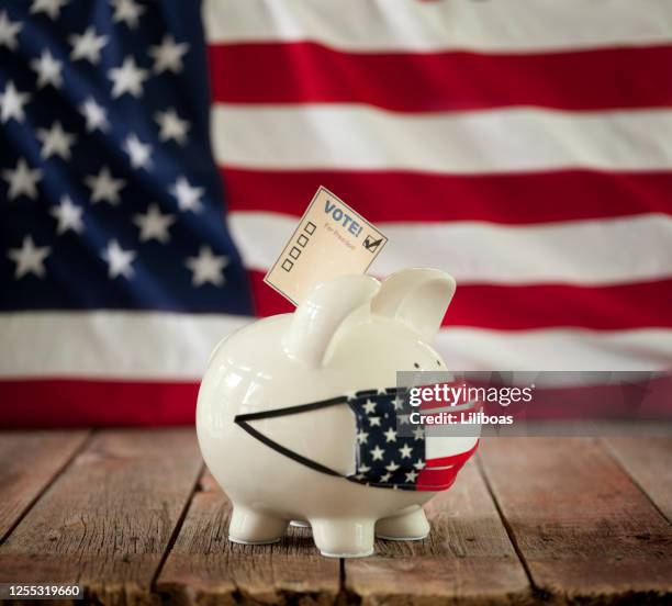 piggy bank with voting ballot and mask on against an american flag background - ballot box money stock pictures, royalty-free photos & images