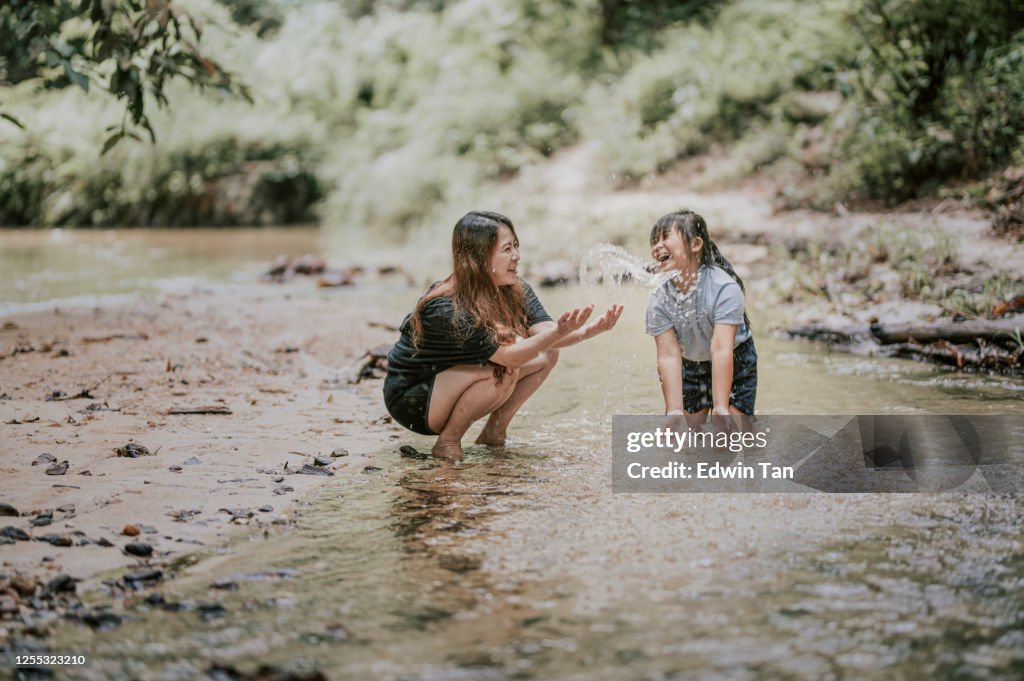 An asian chinese woman having bonding tine with her daughter at the river playing with water splashing