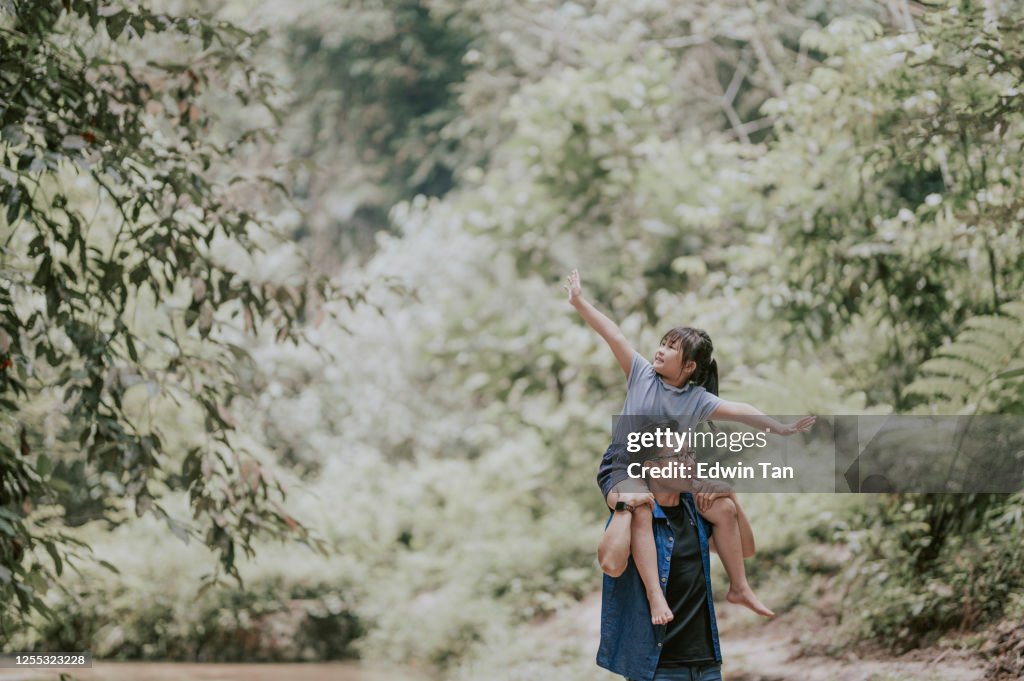 An asian chinese father carrying his daughter on shoulder in the jungle enjoying bonding time together at the river during weekend leisure time