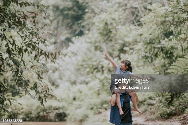 an asian chinese father carrying his daughter on shoulder in the jungle enjoying bonding time together at the river during weekend leisure time - carrying on shoulders stock pictures, royalty-free photos & images