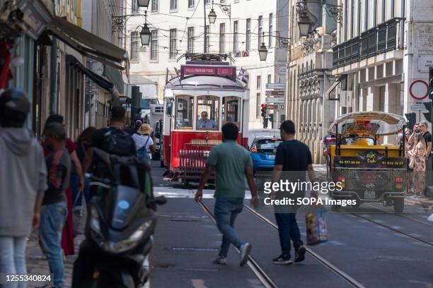 Several people are seen walking near a tram that runs along one of the main streets of the Baixa neighborhood in Lisbon.