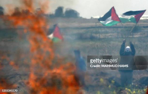 Palestinian youths wave their national flag and set tyres on fire as they clash with Israeli soldiers at the border fence near Gaza City on March 30,...