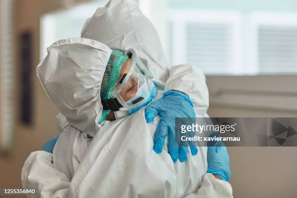 medical team in protective workwear embracing in support - state of emergency stock pictures, royalty-free photos & images