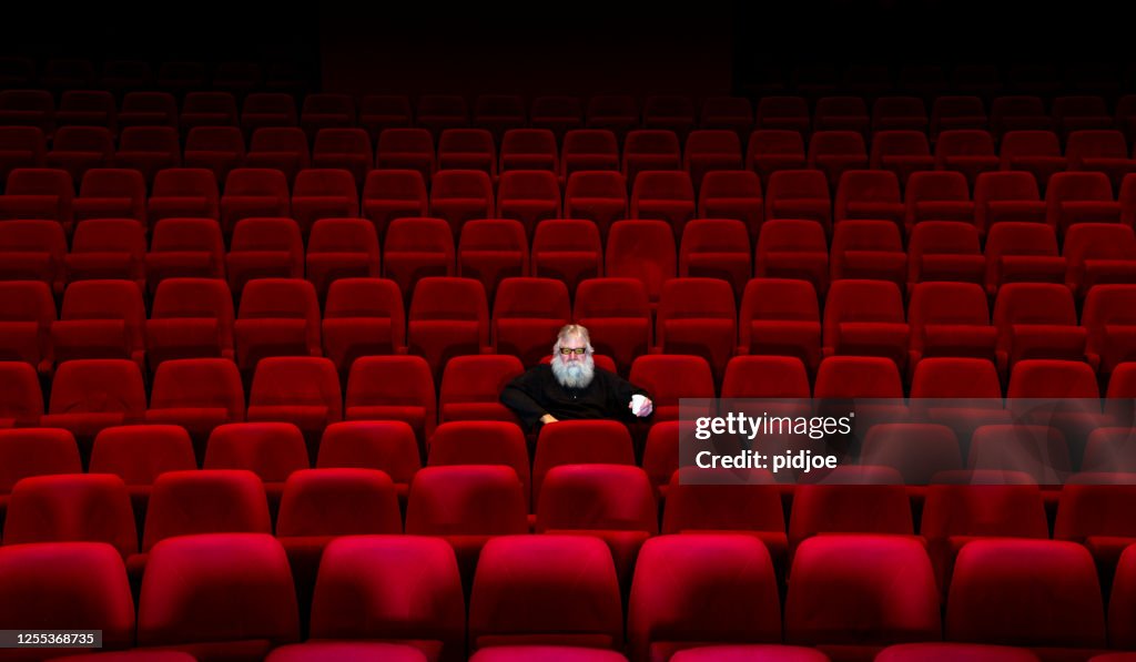 One man with white beard sits in Empty cinema or theatre