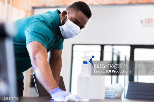 uomo d'affari pulisce il tavolo delle conferenze durante la pandemia di covid-19 - bidello foto e immagini stock