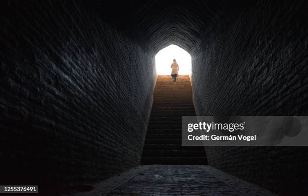 woman walks confidently up stairs coming out from dark tunnel into bright light, yazd, iran - the end imagens e fotografias de stock