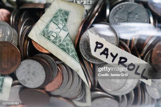 close-up of coins and banknotes in jar labeled payroll - gehaltsstreifen stock-fotos und bilder