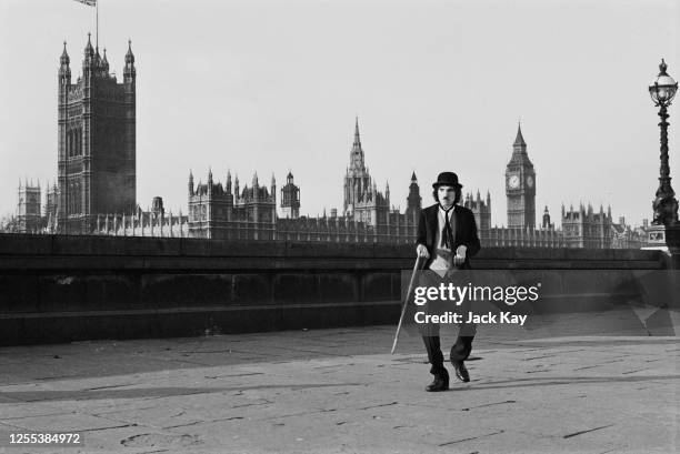 American musician Ron Mael, of Sparks, on the Albert Embankment, London, dressed as Charlie Chaplin's 'Tramp' character, 1972. In the background is...