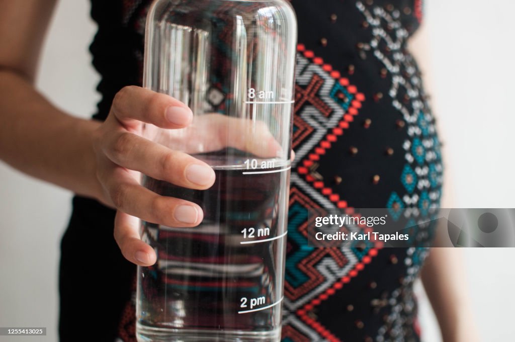A young pregnant woman is holding a reusable water bottle with time stamp