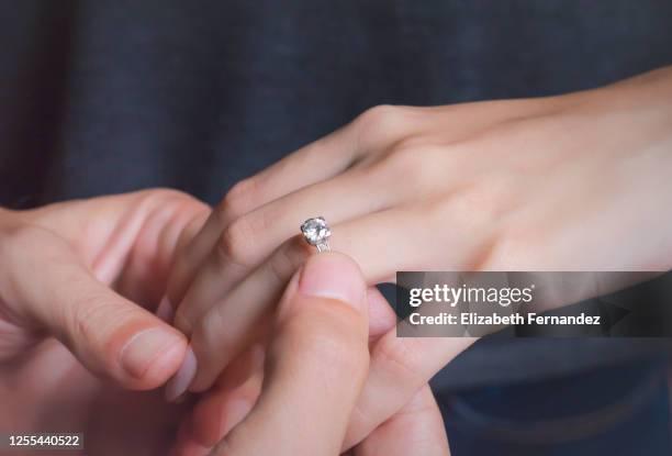 man putting engagement ring on his girlfriend’s finger - man proposing indoor stock-fotos und bilder