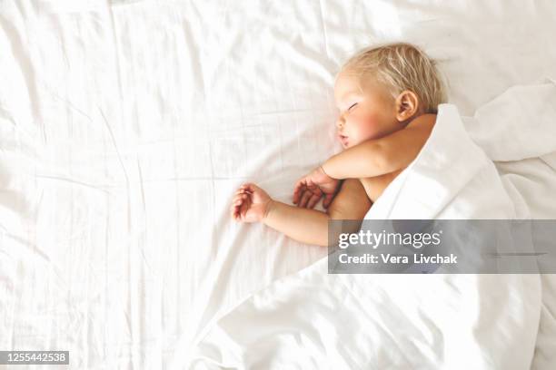 peaceful baby lying on a bed while sleeping in a bright room - baby blankets stockfoto's en -beelden