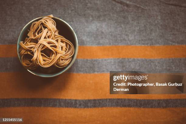 wholemeal tagliatelle in a bowl on a kitchen linnen tablecloth - wholegrain pasta stock pictures, royalty-free photos & images