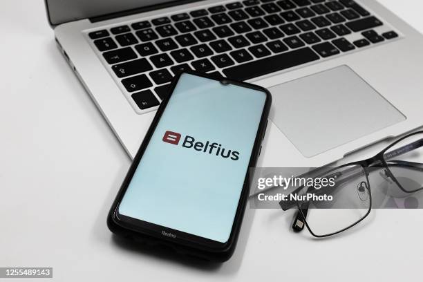 In this photo illustration a Belfius bank logo is displayed on a smartphone screen above a Macbook next to glasses in Athens, Greece on May 17, 2023.