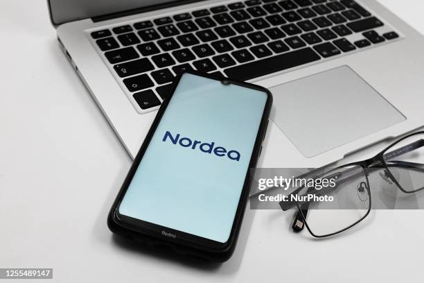 In this photo illustration a Nordea bank logo is displayed on a smartphone screen above a Macbook next to glasses in Athens, Greece on May 17, 2023.