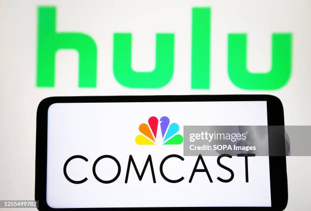 In this photo illustration, Comcast Corporation logo is seen on a smartphone and Hulu logo on a pc screen.