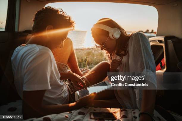 young couple in the car trunk on vacation.sea and sunset in background - cell phone using beach stock pictures, royalty-free photos & images