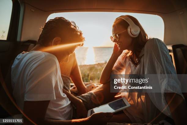 young couple in the car trunk on vacation.sea and sunset in background - car listening to music imagens e fotografias de stock