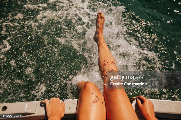 junge frau sitzt auf einem boot und spritzt auf dem wasser - girls sunbathing stock-fotos und bilder