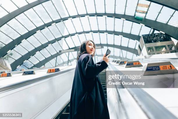 young business woman using smart phone, riding an escalator - escalator stock-fotos und bilder