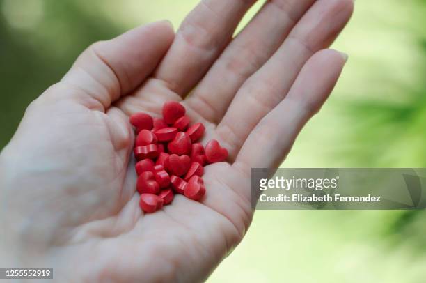 hand of woman holding heart shaped pills - heart pill stockfoto's en -beelden