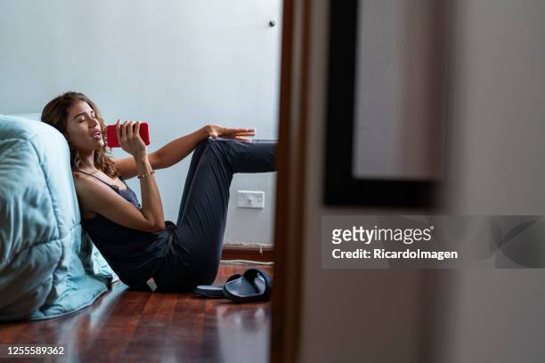 Young woman sings while listening to her favorite song sitting on the floor in her room