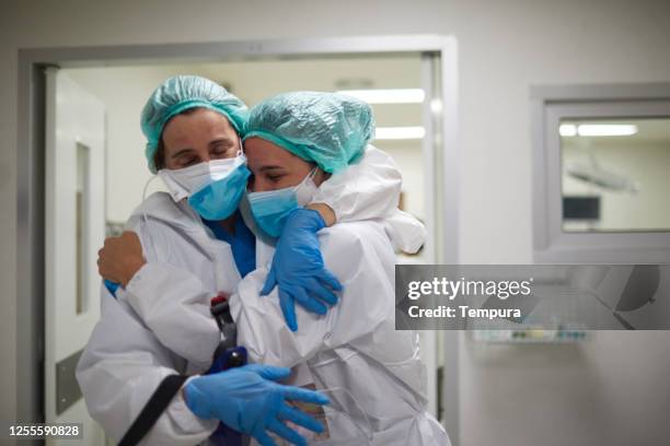 two healthcare workers hug in celebration of a successful surgery procedure - hospital teamwork stock pictures, royalty-free photos & images