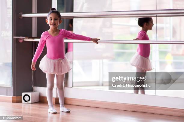 süße kleine ballerina hält auf schiene während des unterrichts lächelnd vor der kamera - ballett mädchen stock-fotos und bilder