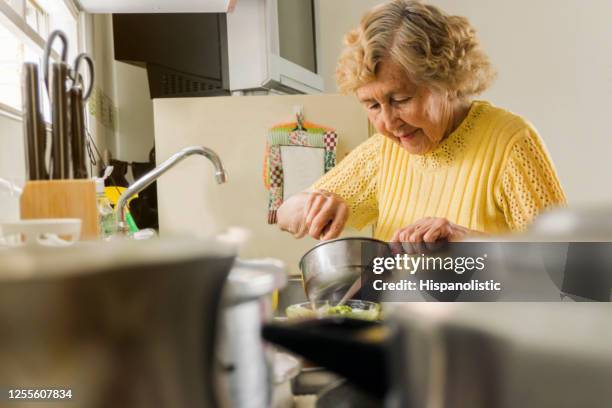 latin american woman preparing lunch at home looking very focused - senior cooking stock pictures, royalty-free photos & images