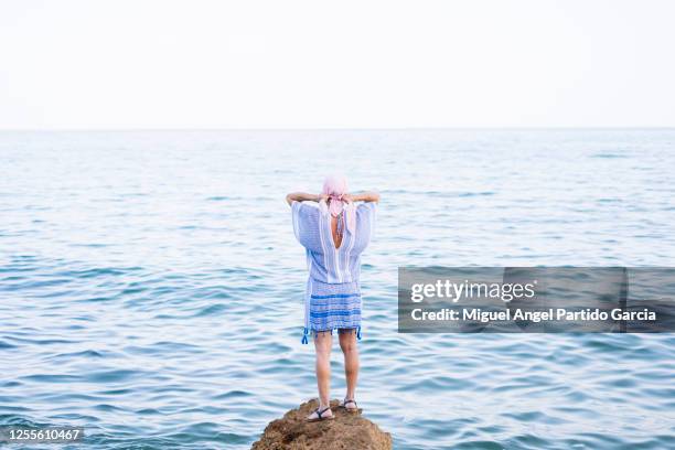 woman with cancer scarf is on a rock near the sea. - cancerland 2019 bildbanksfoton och bilder