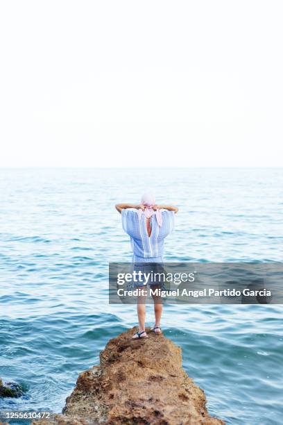 woman with cancer scarf is on a rock near the sea. - cancerland 2019 bildbanksfoton och bilder