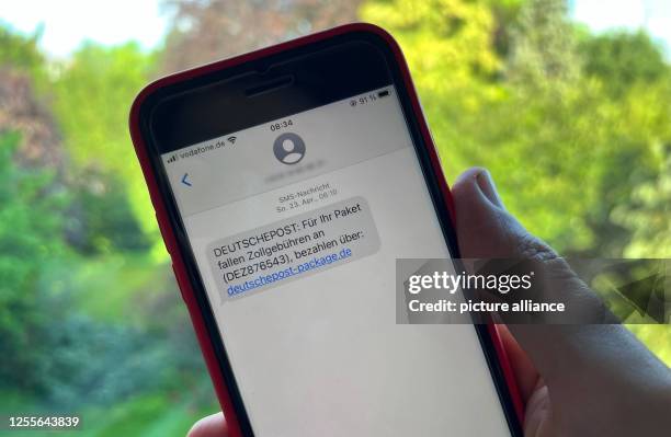 May 2023, North Rhine-Westphalia, Duesseldorf: A man holds a smartphone with a fraudulent SMS. There has been a sharp increase in the number of...