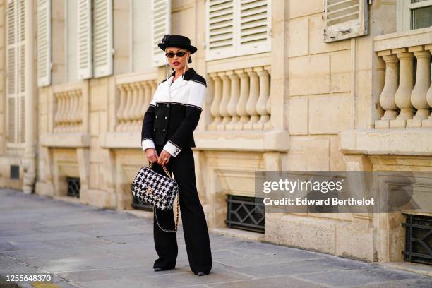 Lexi Fargo wears a black hat with an attached Chanel flower, Chanel golden and red earrings, Chanel sunglasses with pearls, a hair bow ribbon, a...