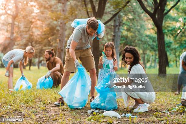 parents cleaning up garbage from the park with their little daughter - biodegradable stock pictures, royalty-free photos & images